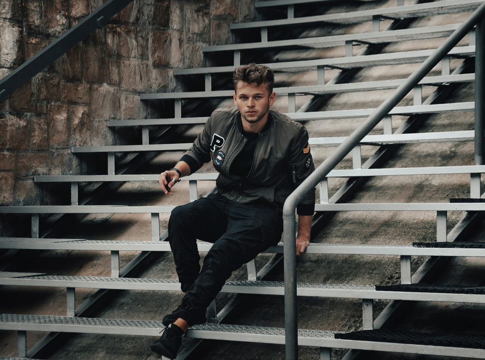 man in black jacket and black pants sitting on gray concrete staircase
