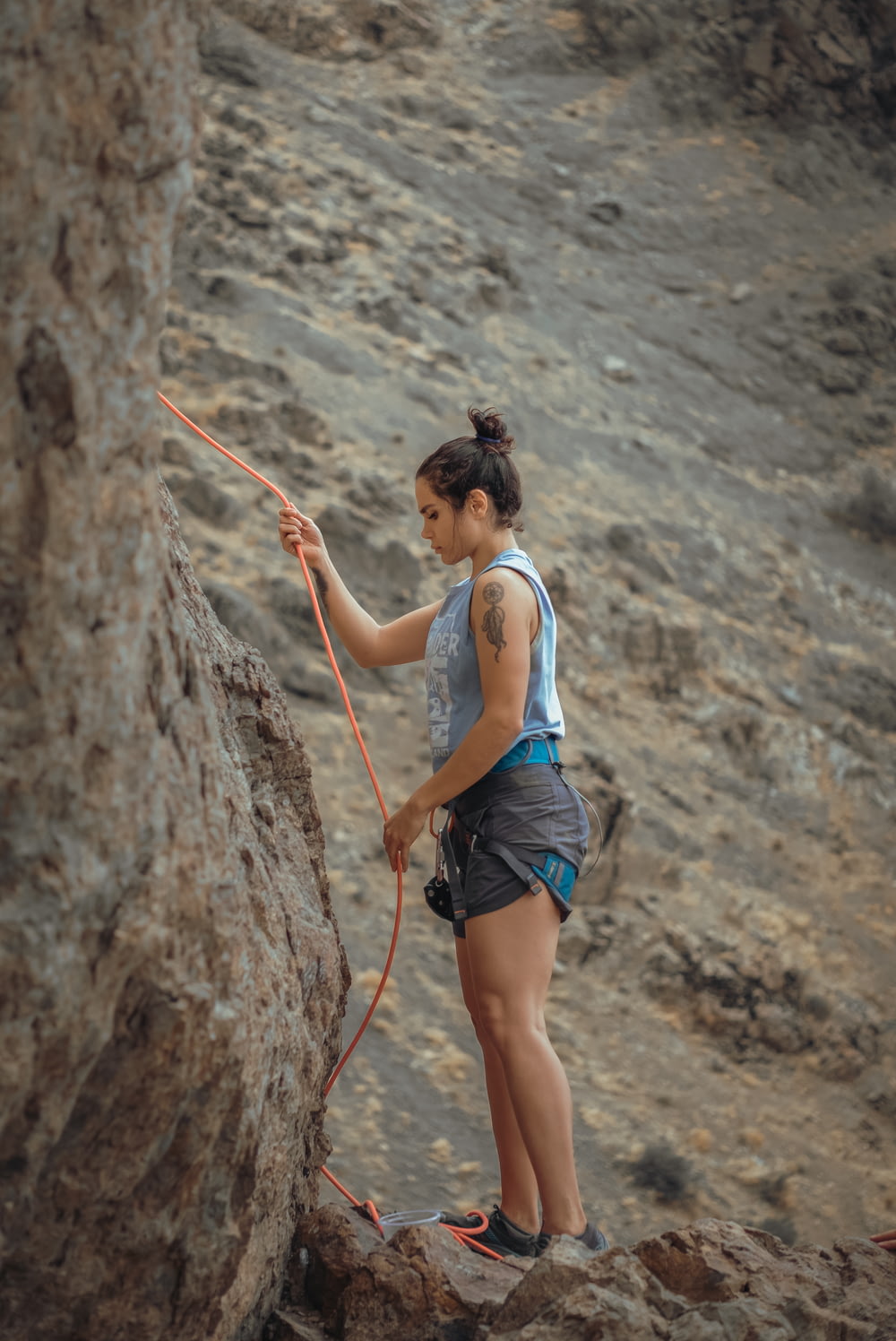 woman in white tank top and blue denim shorts climbing on brown rock during daytime