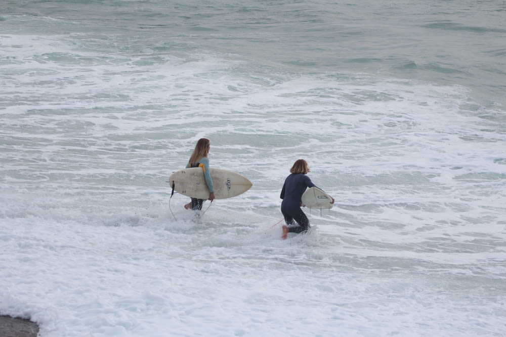 2 men and woman holding white and blue surfboard on sea during daytime