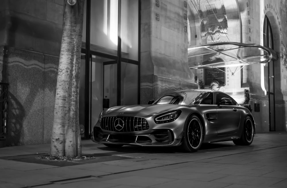 Foto in scala di grigi della Mercedes Benz Coupé parcheggiata accanto all'edificio