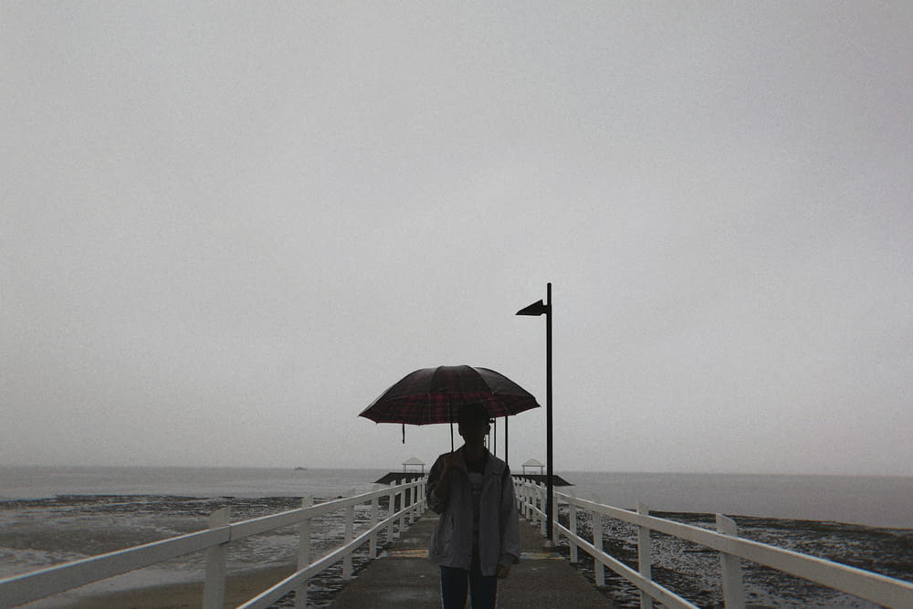 person in black jacket and pants holding umbrella standing on dock during daytime