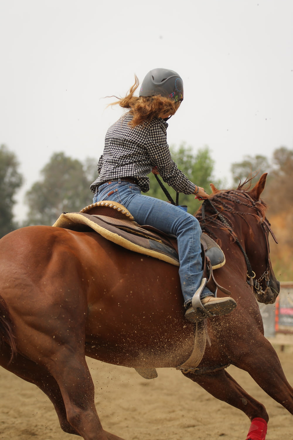 Mujer con camisa de manga larga a rayas azules y blancas montando caballo marrón durante el día