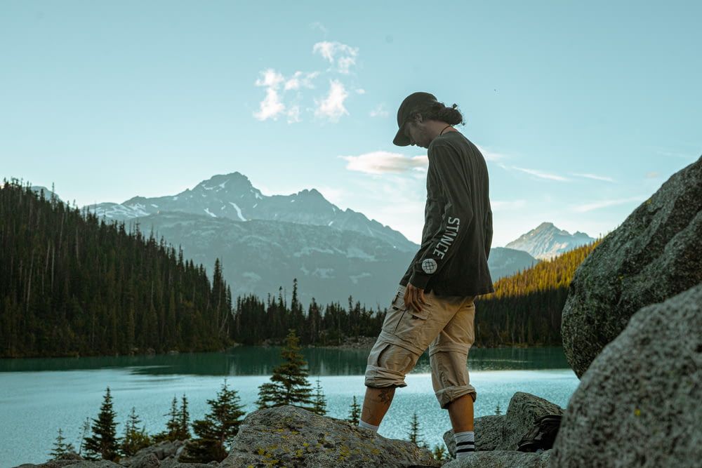 man in black hoodie and brown pants standing on rock near lake during daytime