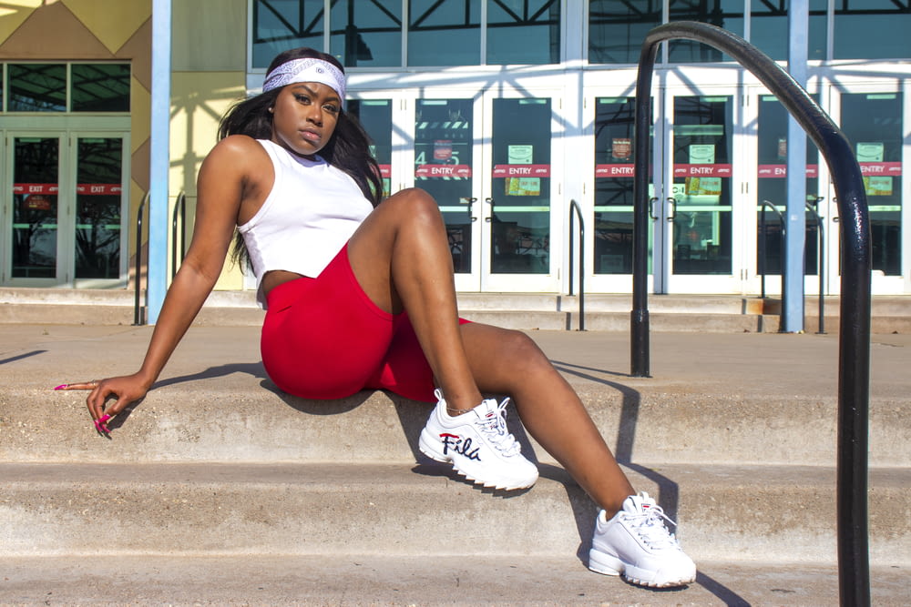 woman in red tank top and white nike sneakers sitting on concrete bench during daytime