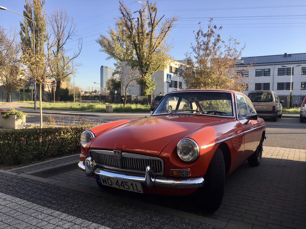 red classic car parked on roadside near bare trees during daytime