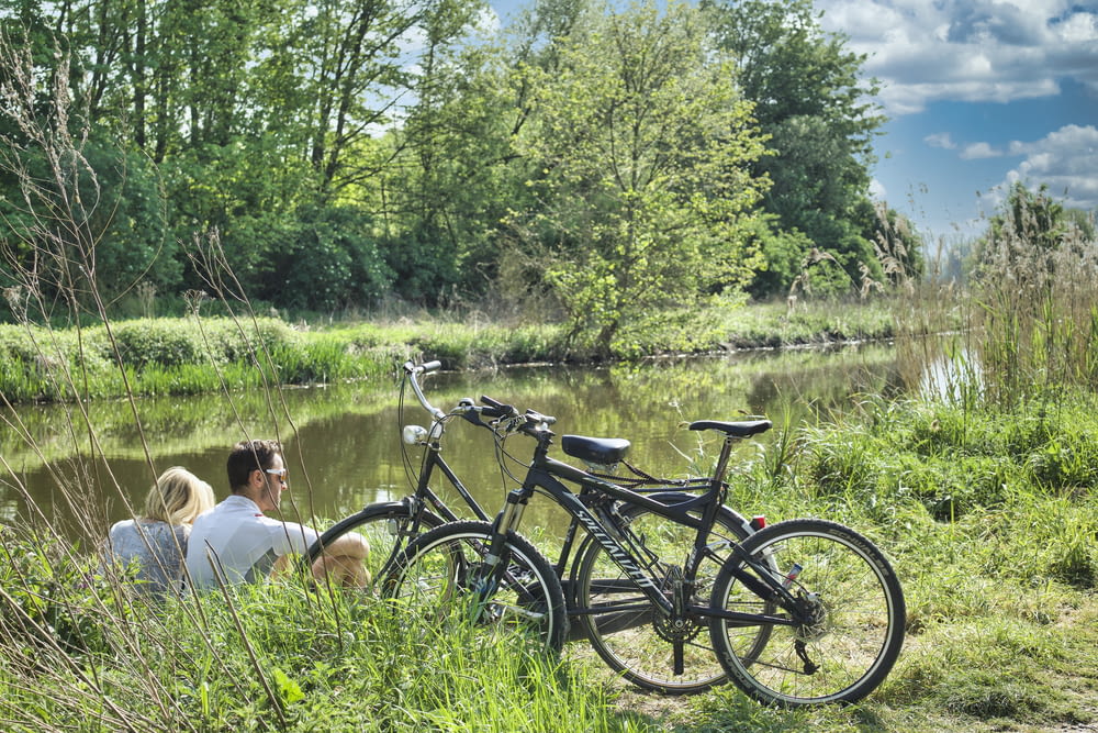 man and woman sitting on grass field beside black bicycle during daytime