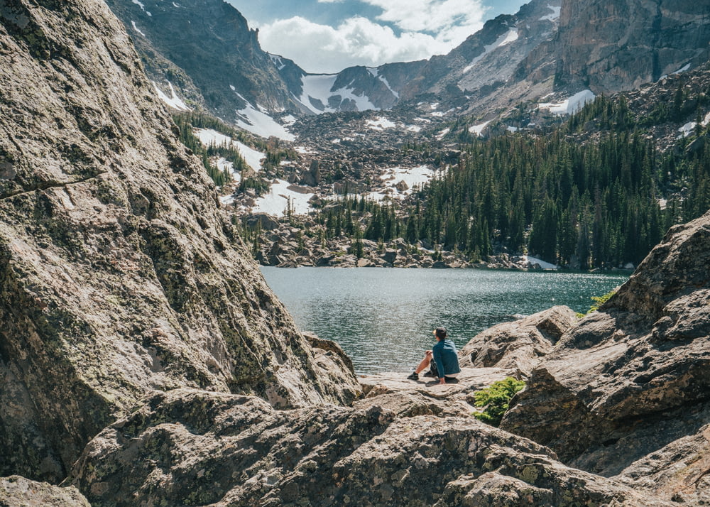 호수와 산맥 근처의 바위에 앉아있는 사람