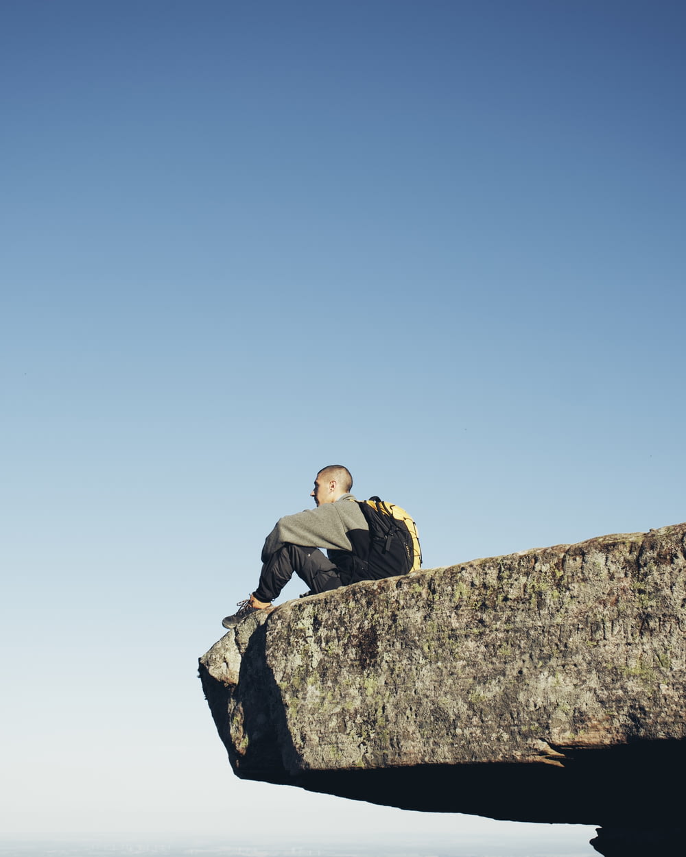 man in black jacket sitting on gray rock during daytime