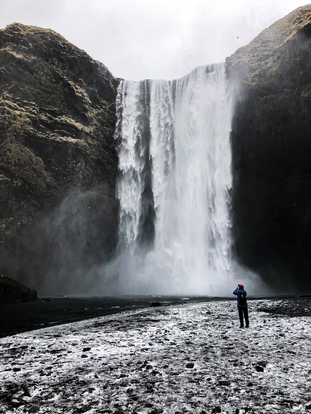 man in blue jacket standing near waterfalls during daytime