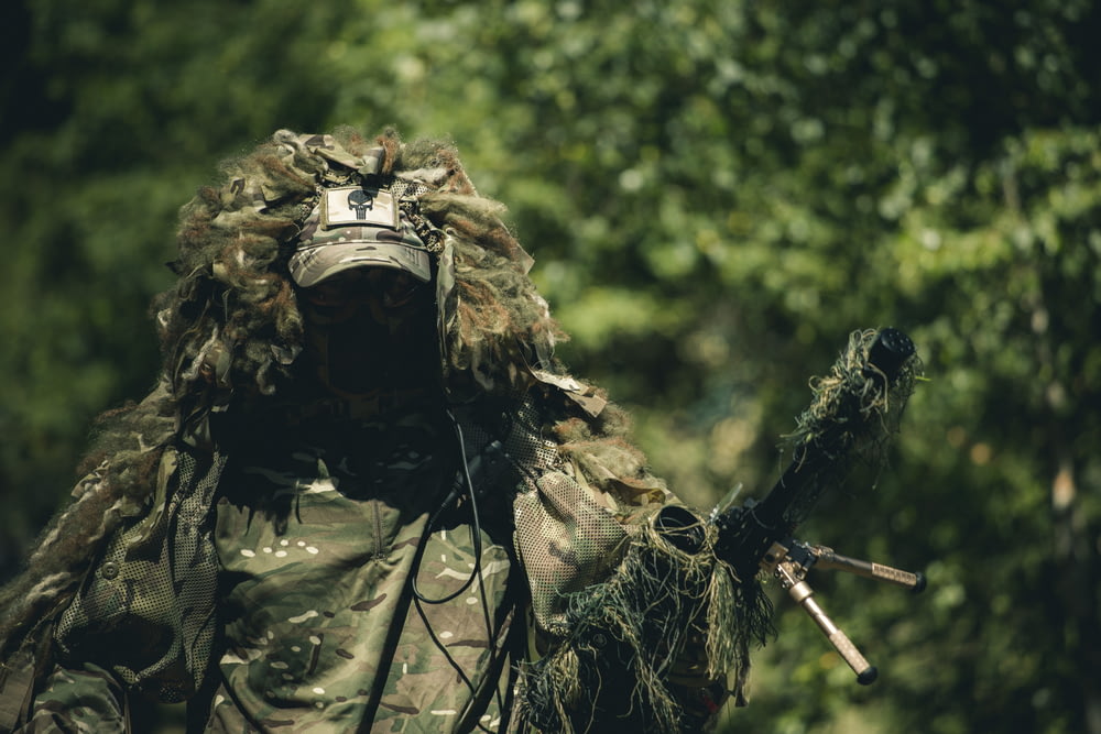 homem em uniforme de camuflagem verde e marrom segurando rifle