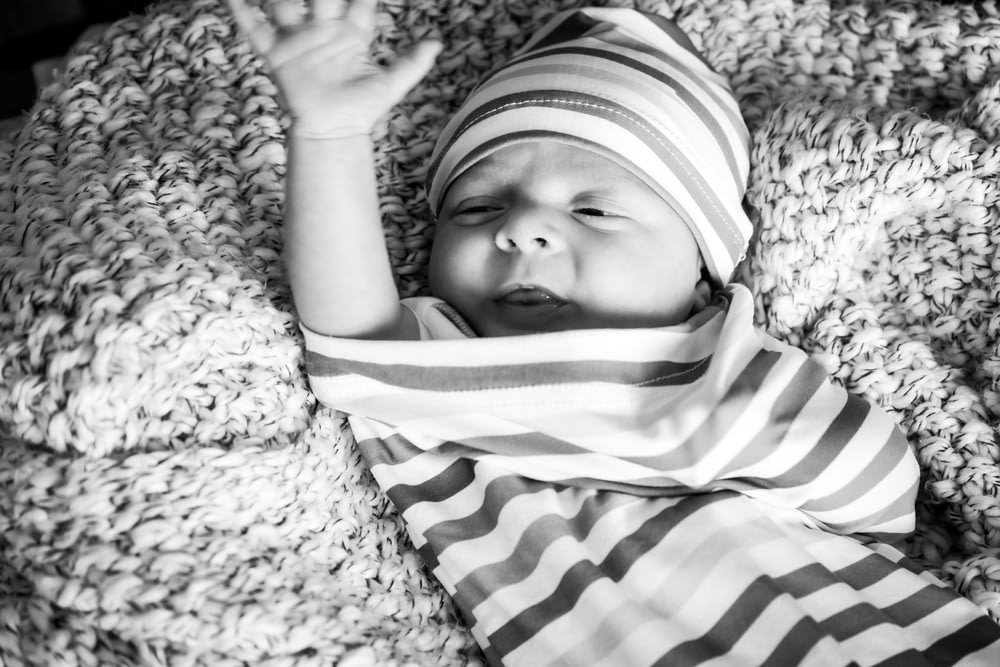 grayscale photo of baby in stripe shirt lying on the ground