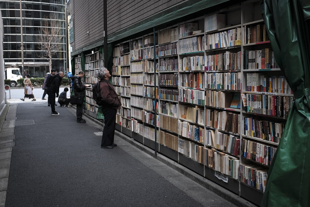 man in black jacket standing near books in book shelves