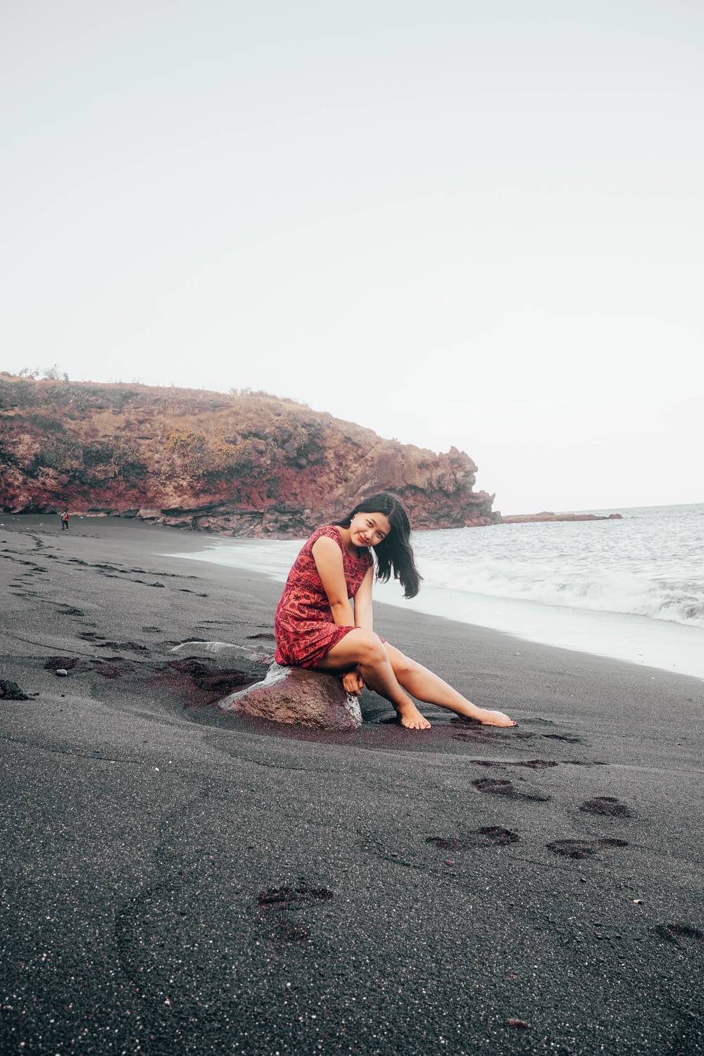 woman in red dress sitting on beach shore during daytime