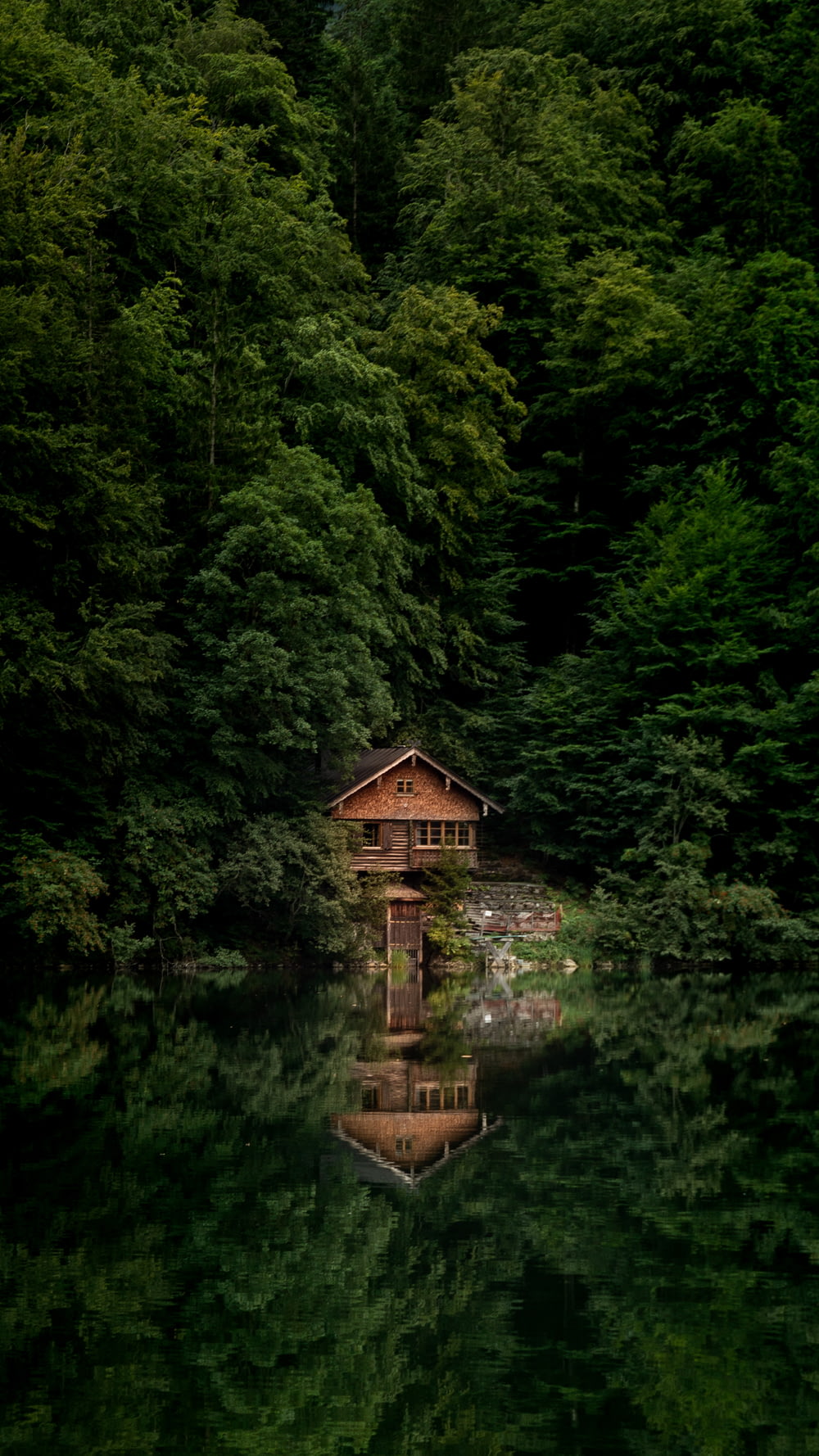 Braunes Holzhaus auf Gewässer, tagsüber umgeben von grünen Bäumen