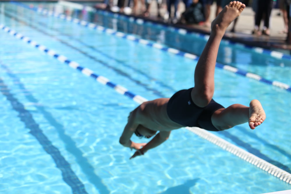 femme en maillot de bain noir une pièce sautant sur la piscine pendant la journée