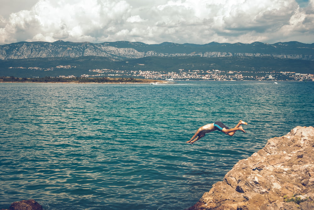 person jumping on rocky shore during daytime