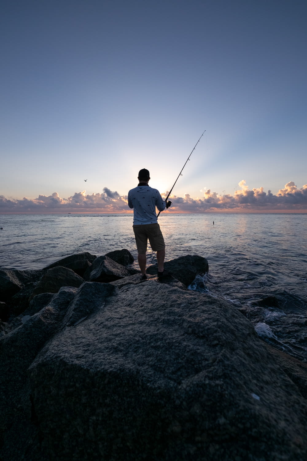 Mann in weißem Hemd und braunen Shorts beim Fischen auf See tagsüber