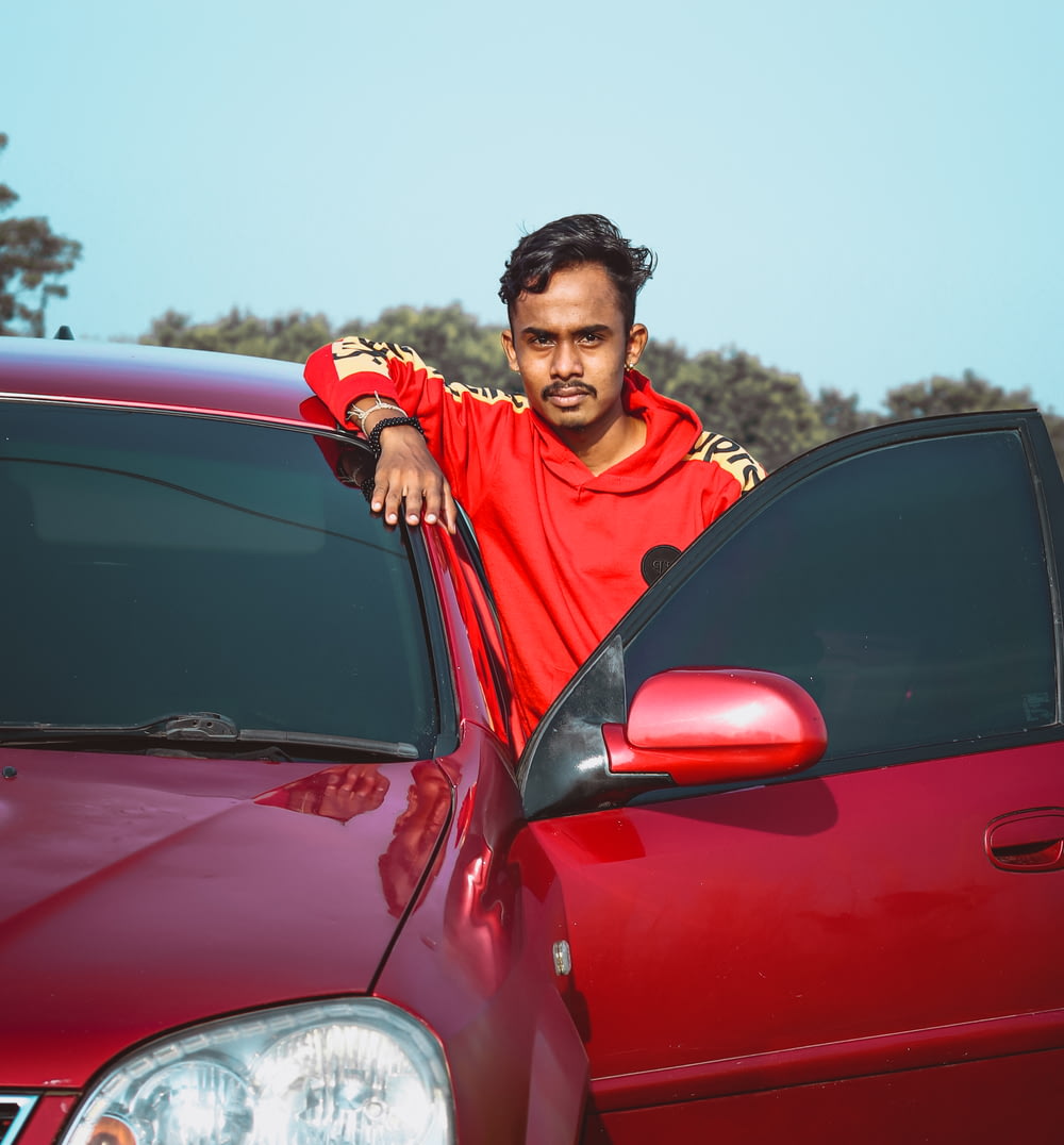 man in red and black hoodie standing beside red car during daytime
