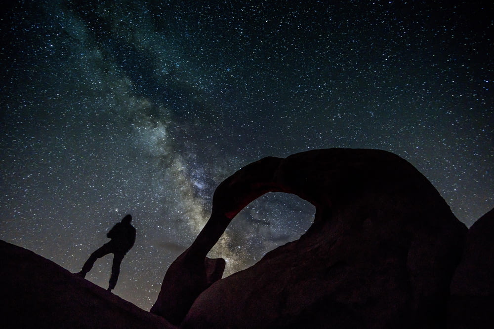 silhouette of man and woman standing on rock formation during night time
