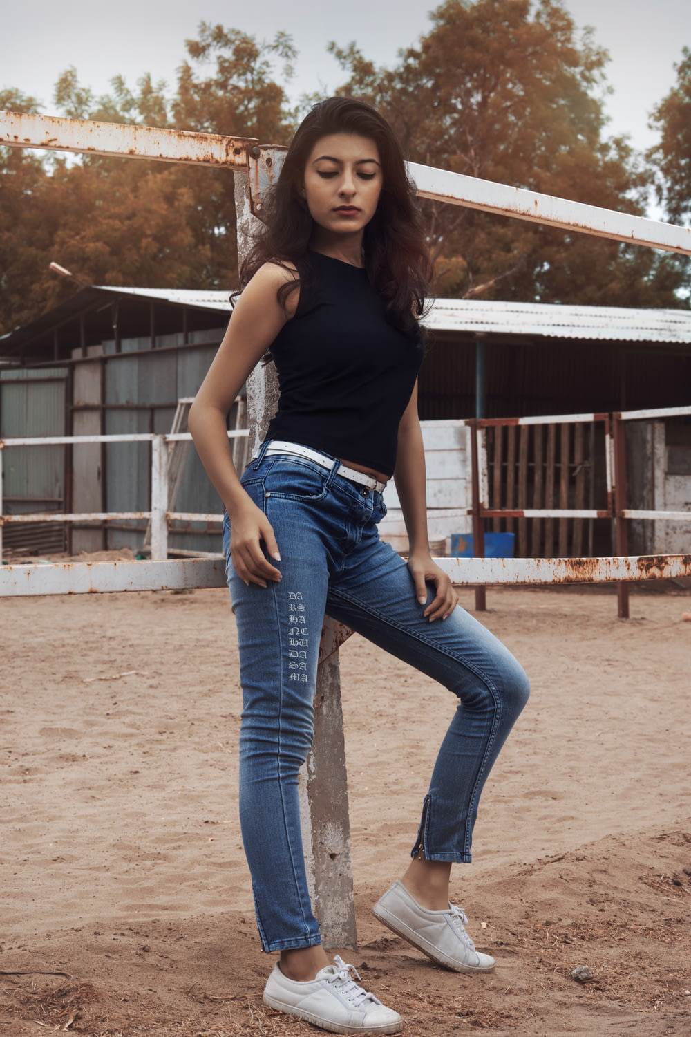 woman in black tank top and blue denim jeans standing on brown sand during daytime