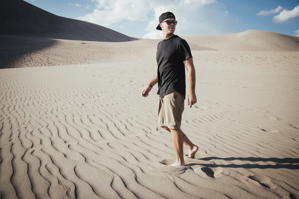 man in black crew neck t-shirt and white shorts standing on brown sand during daytime