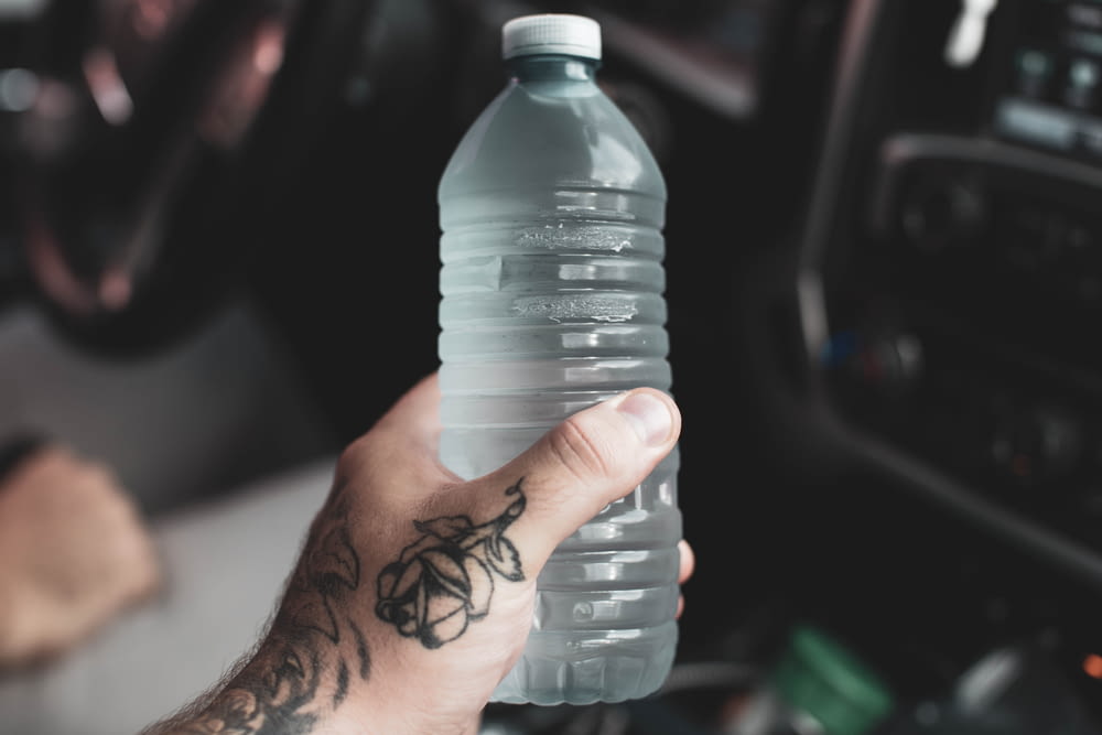 Persona che tiene in mano una bottiglia di plastica trasparente