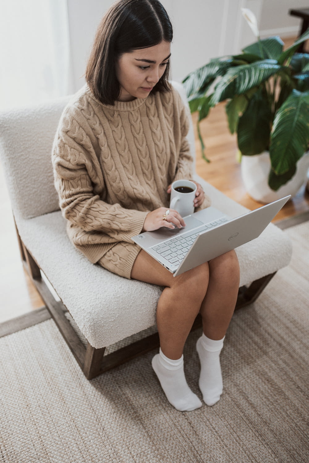 woman in white sweater sitting on couch using laptop