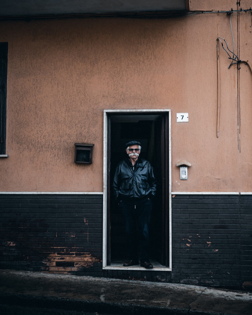 man in black leather jacket standing beside brown wooden door