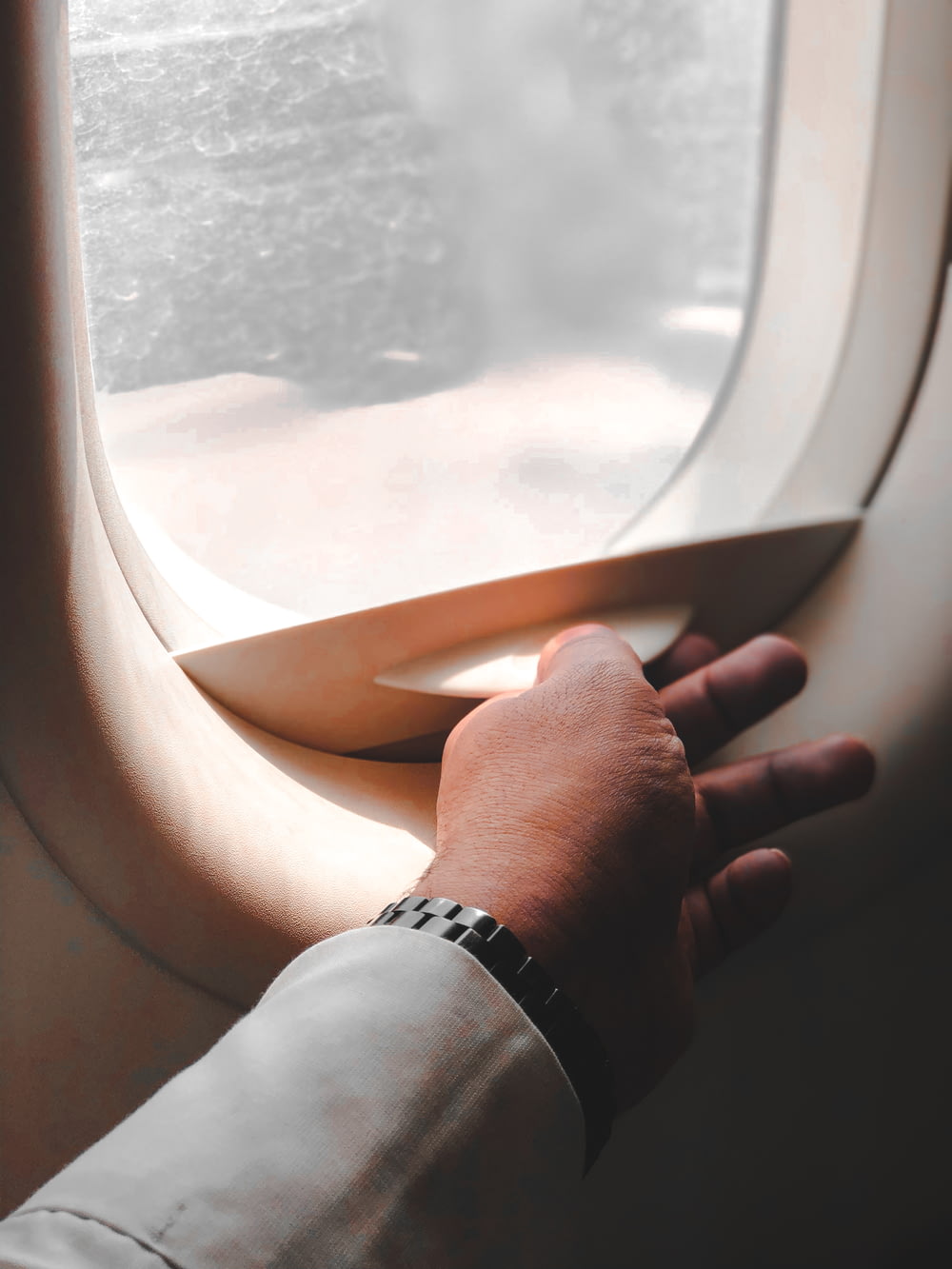 Person, die silberne Armbanduhr trägt, die Flugzeugfenster hält