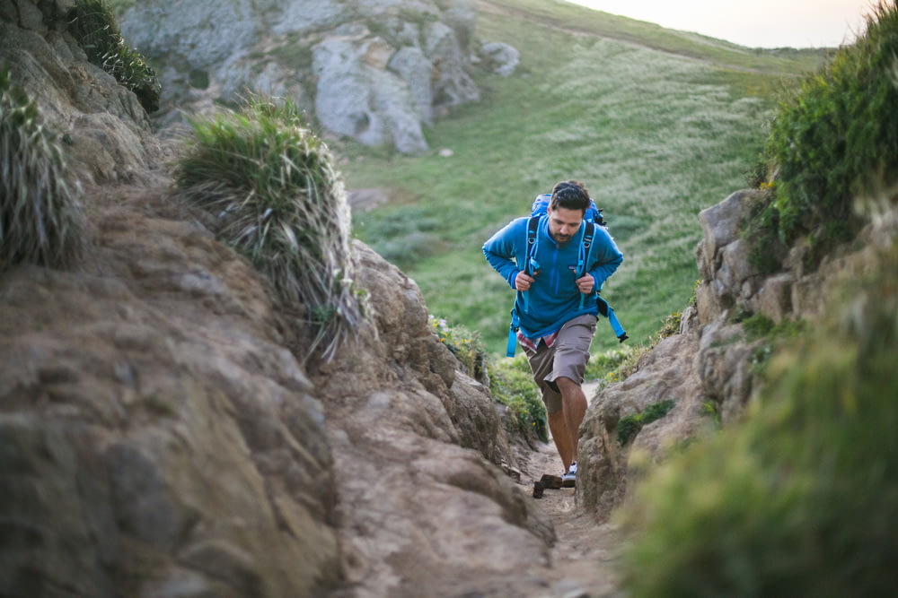homem de camiseta azul e shorts azuis correndo na montanha rochosa marrom durante o dia