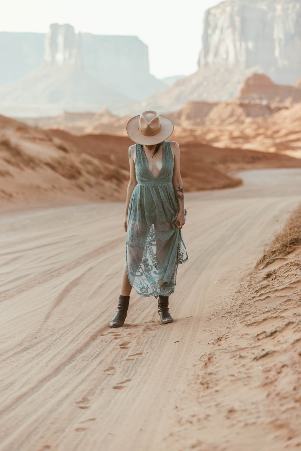 昼間、茶色の砂の上を歩く緑のタンクトップと青いスカートの女性