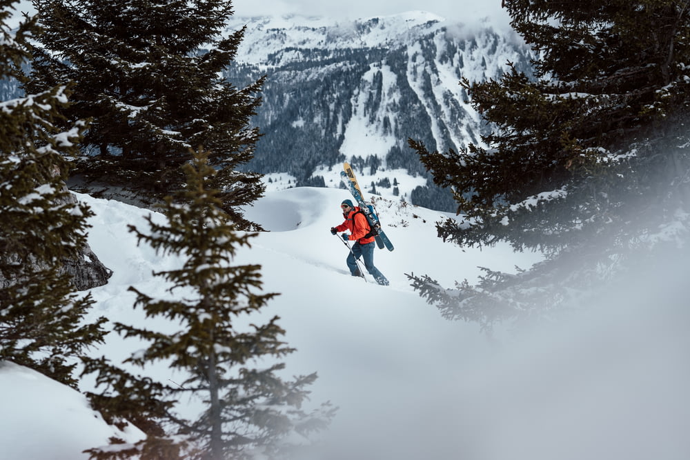 Person in roter Jacke und schwarzer Hose, die tagsüber auf dem Snowboard auf einem schneebedeckten Berg fährt