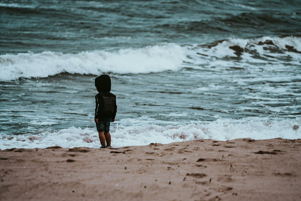 child in black shirt walking on beach during daytime
