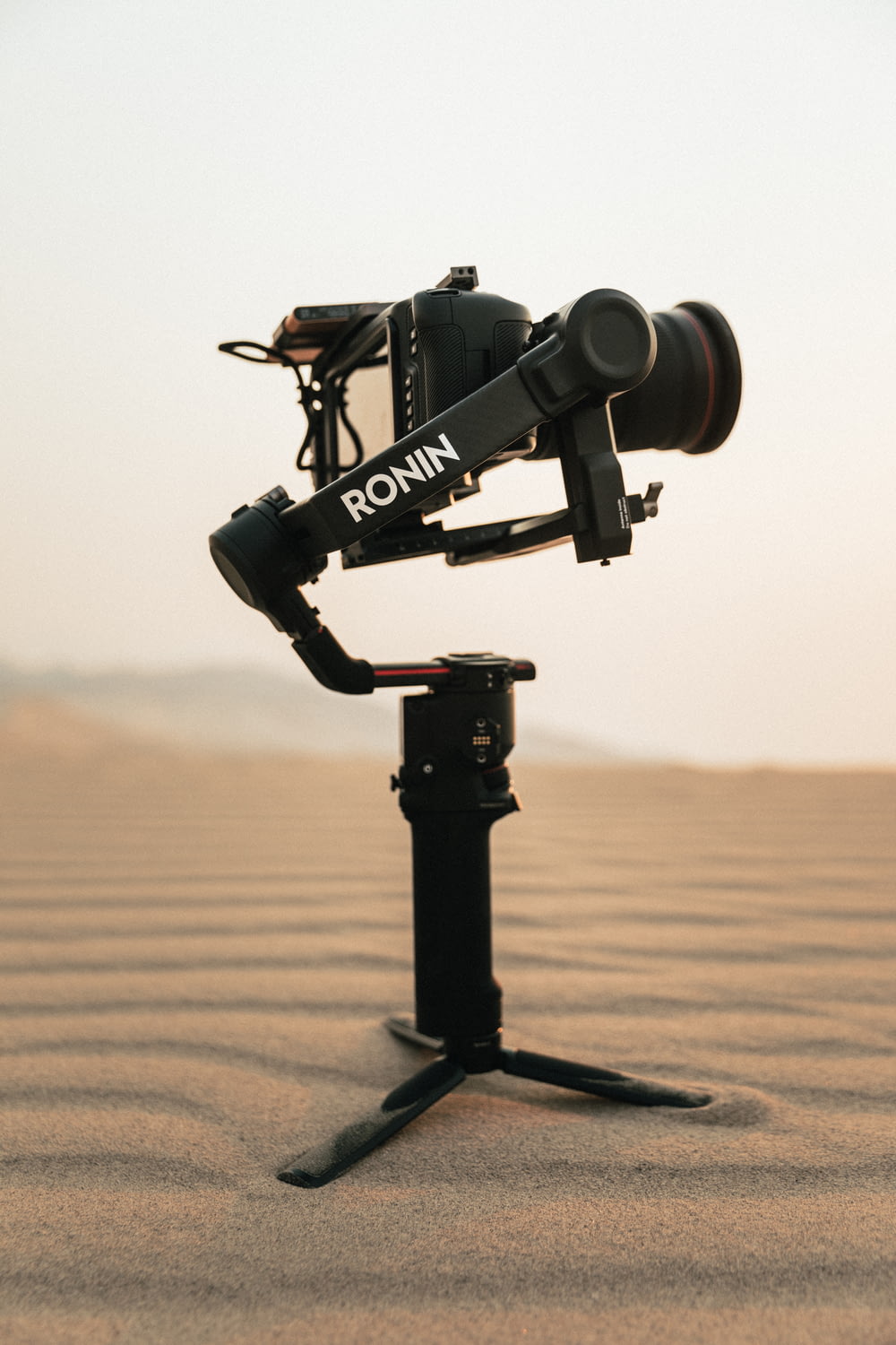 낮 동안 갈색 모래 위에 삼각대에 검은 카메라