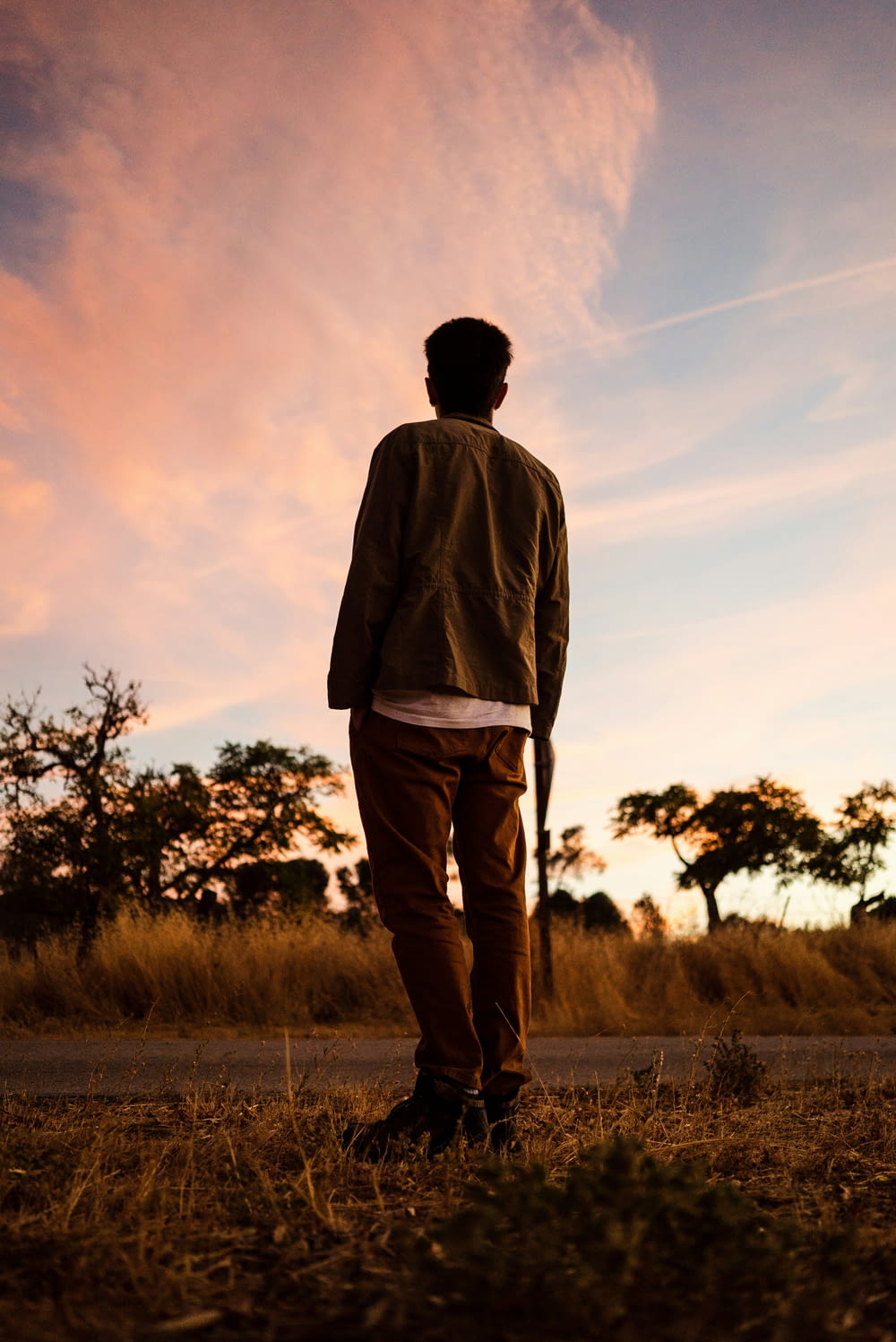 man in gray jacket standing on grass field during sunset