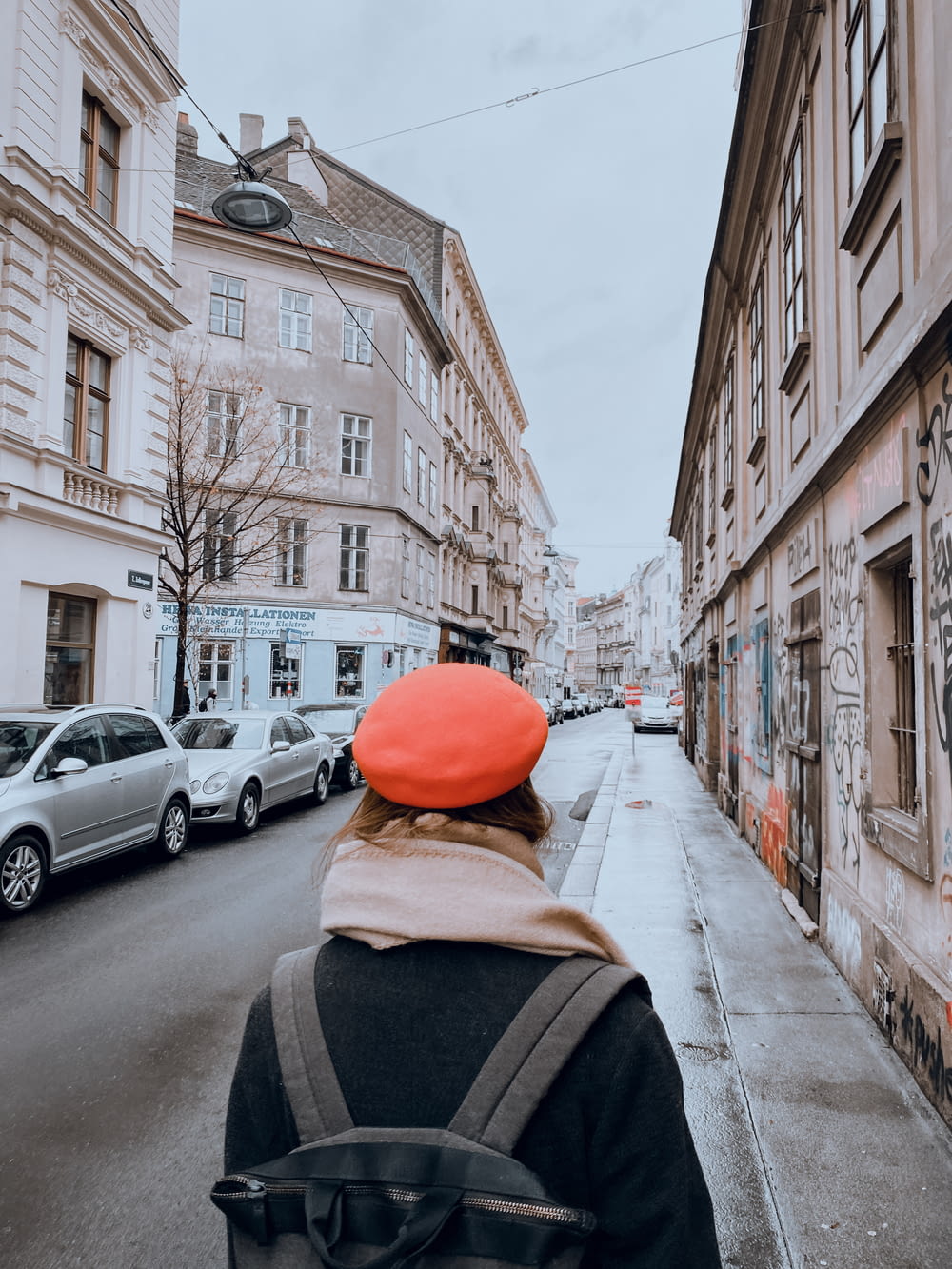person in orange cap and black jacket walking on sidewalk during daytime