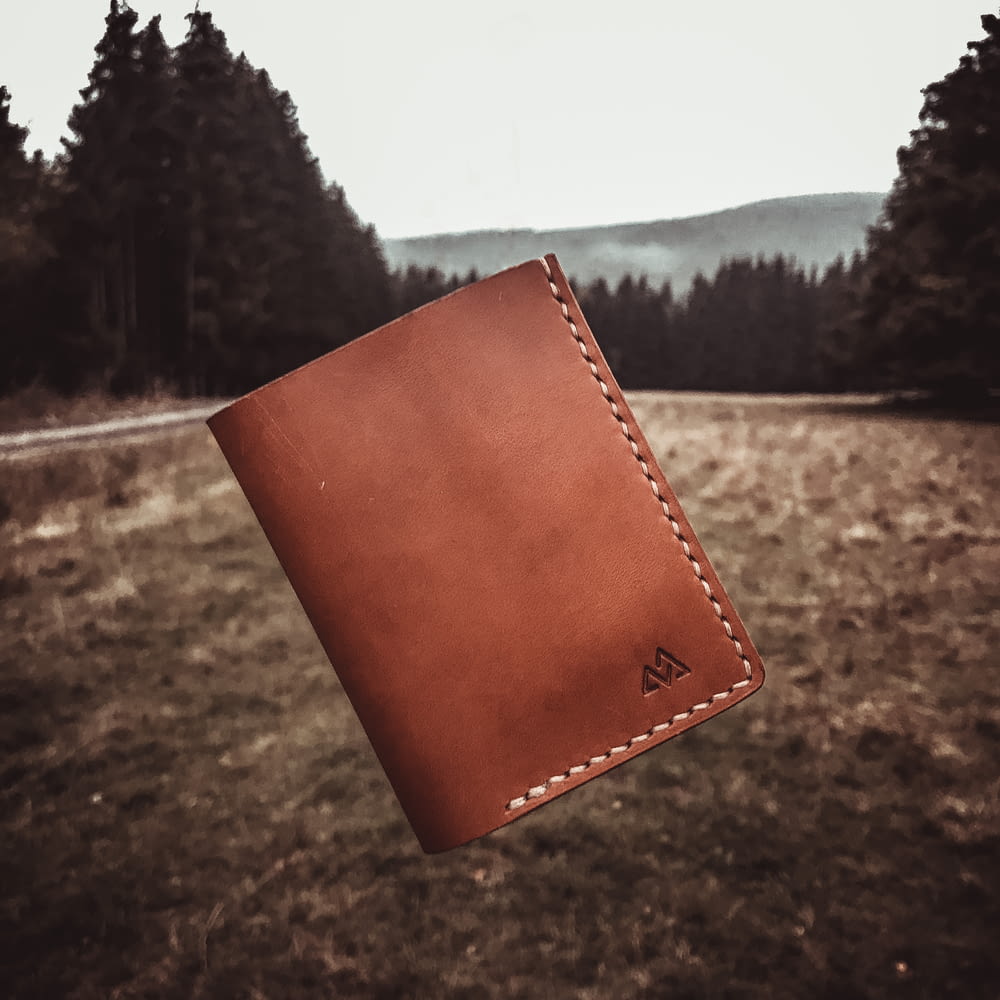 brown leather bifold wallet on brown field during daytime