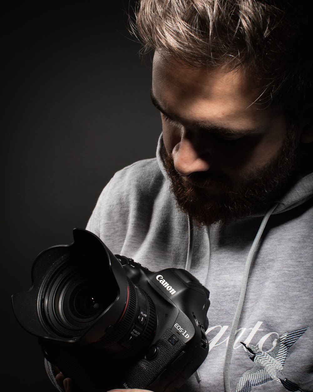 man in gray hoodie holding black nikon dslr camera