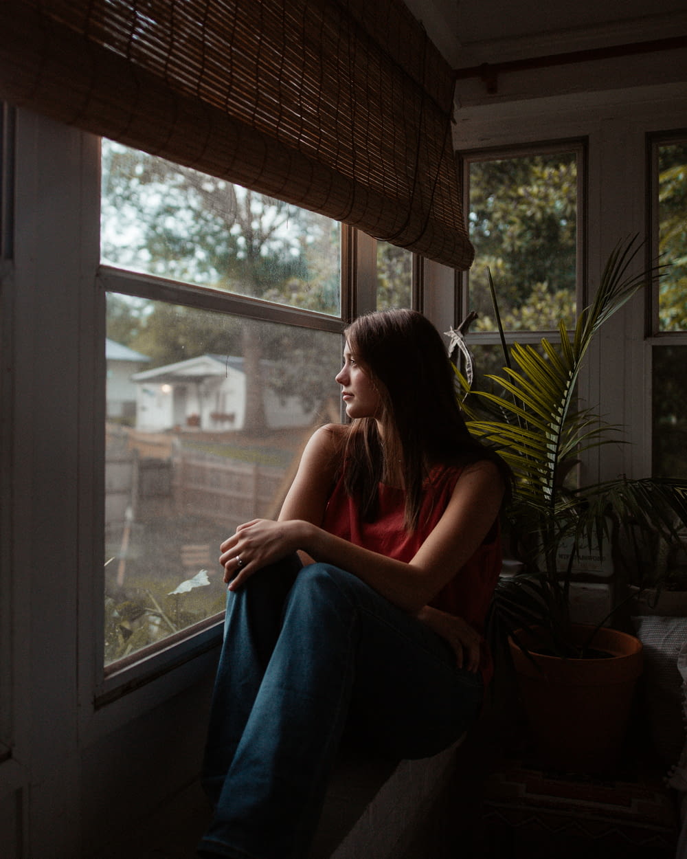 femme en débardeur rouge assise sur la fenêtre