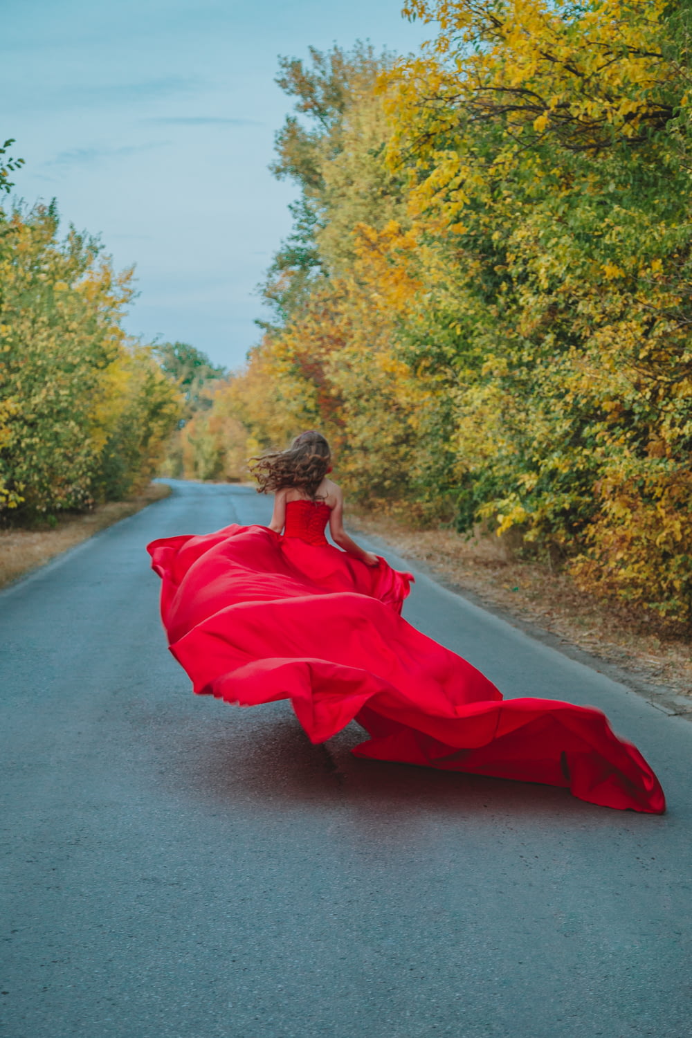 woman in red dress sitting on gray concrete road during daytime