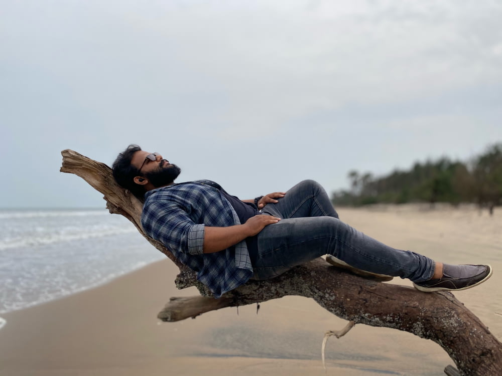 man in black and white plaid shirt and blue denim jeans sitting on brown tree log
