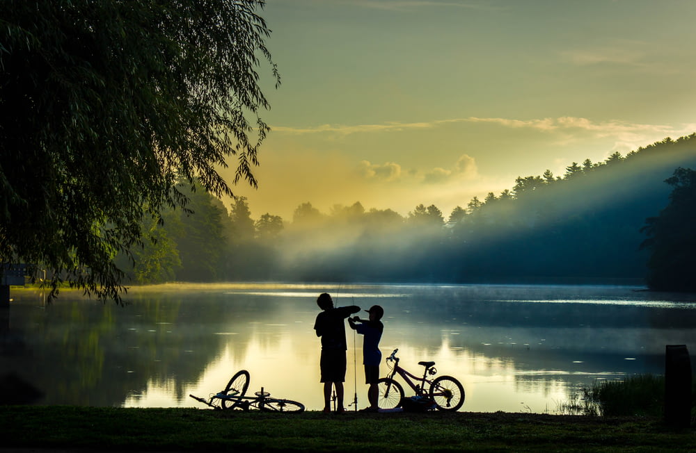 silhouette of 2 people riding bicycle on lake during sunset