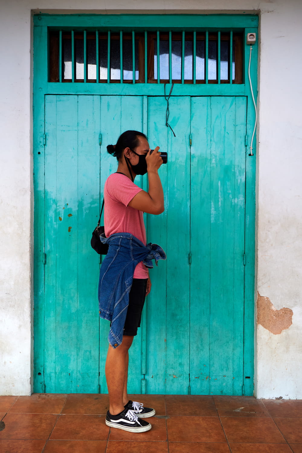 woman in black tank top and blue denim shorts standing beside blue wooden door