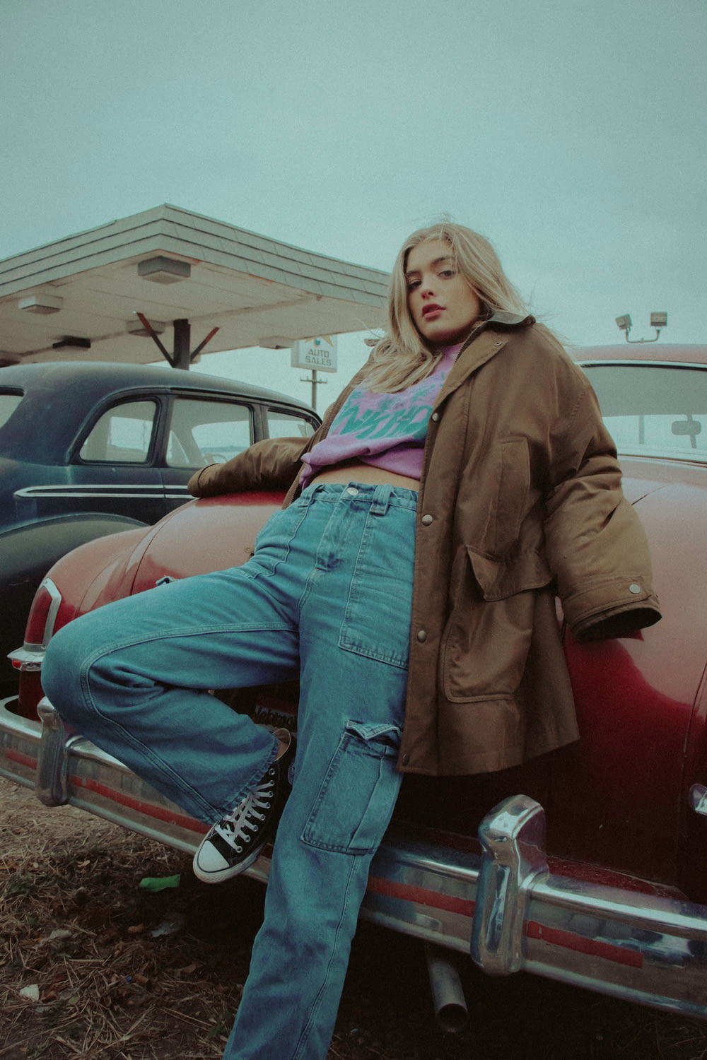 woman in brown jacket and blue denim jeans sitting on red car