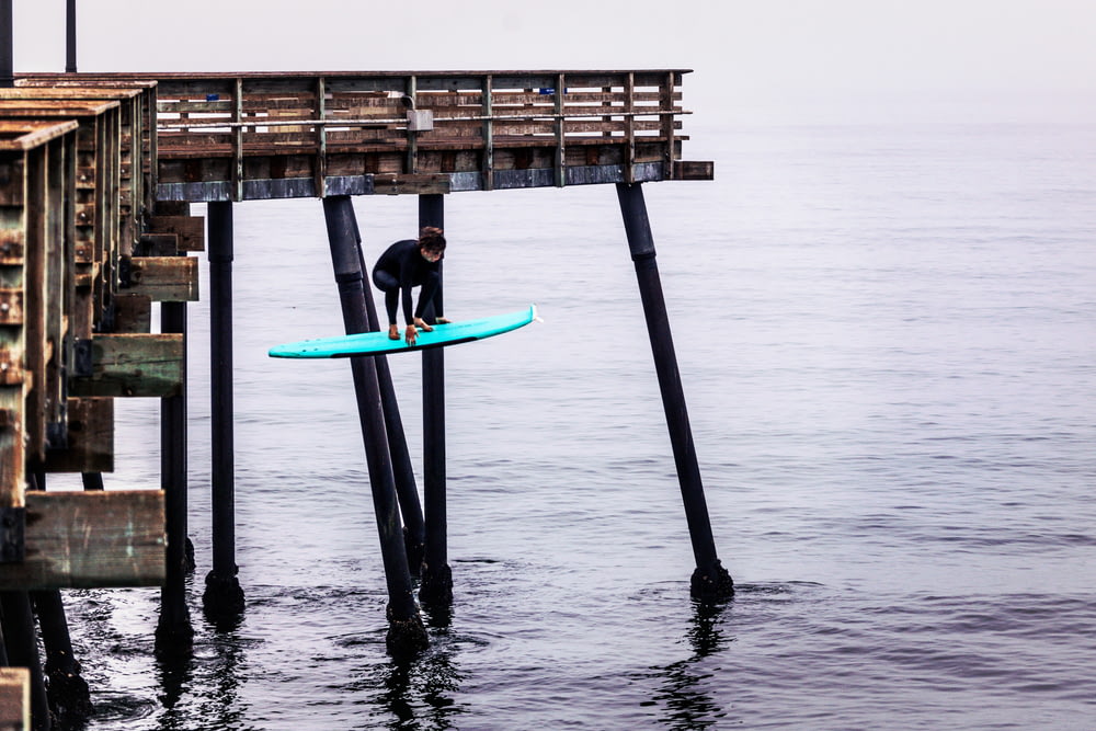 낮 동안 바다에서 파란색 서핑 보드를 들고 검은 잠수복을 입은 사람