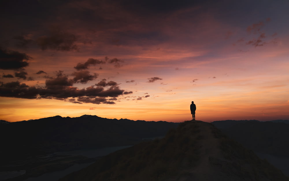 silhouette of person standing on top of mountain during daytime