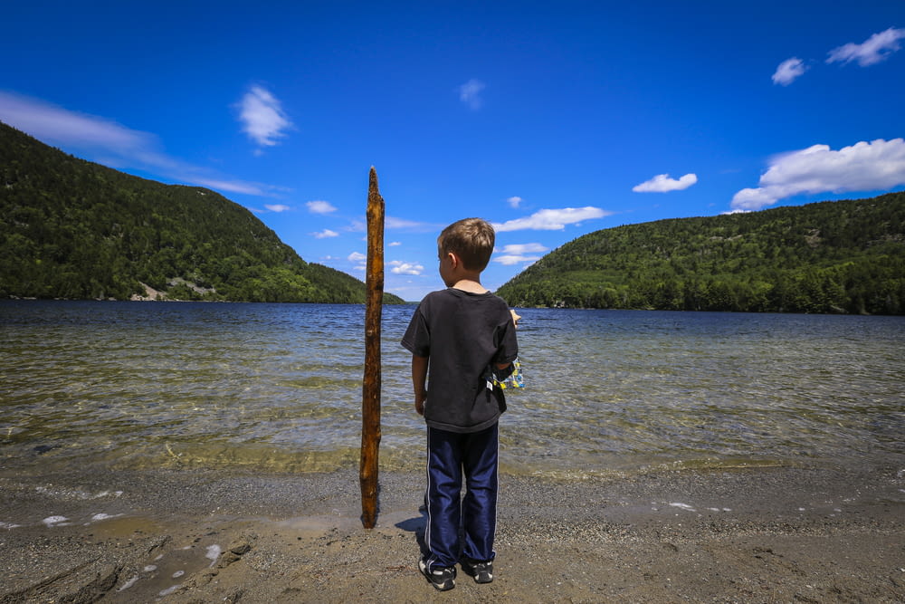 boy in black jacket standing on beach shore during daytime