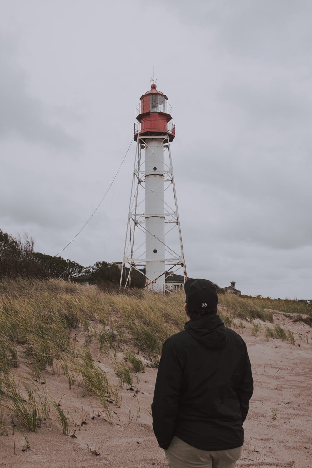 man in black hoodie standing near white and red lighthouse under cloudy sky during daytime