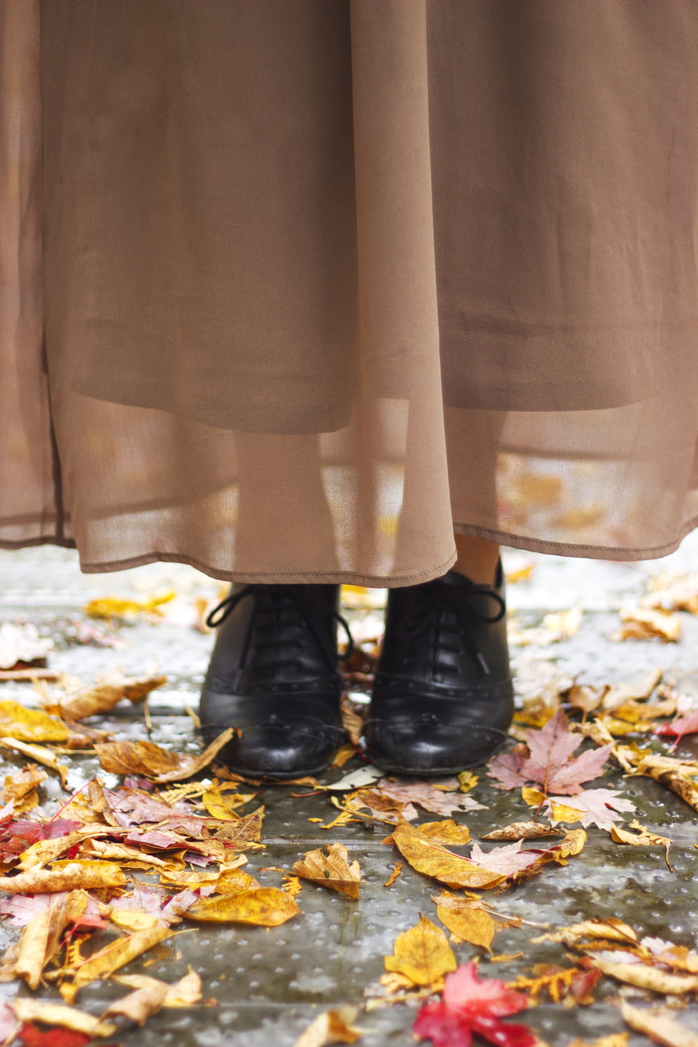 person in black leather boots standing on dried leaves
