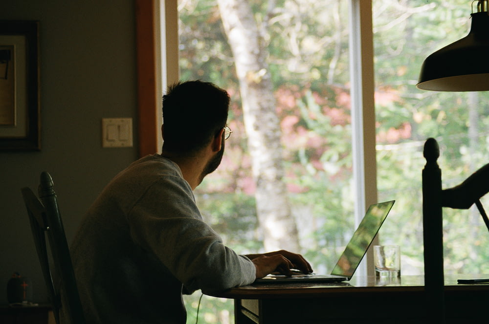 uomo in felpa con cappuccio grigia usando il computer portatile